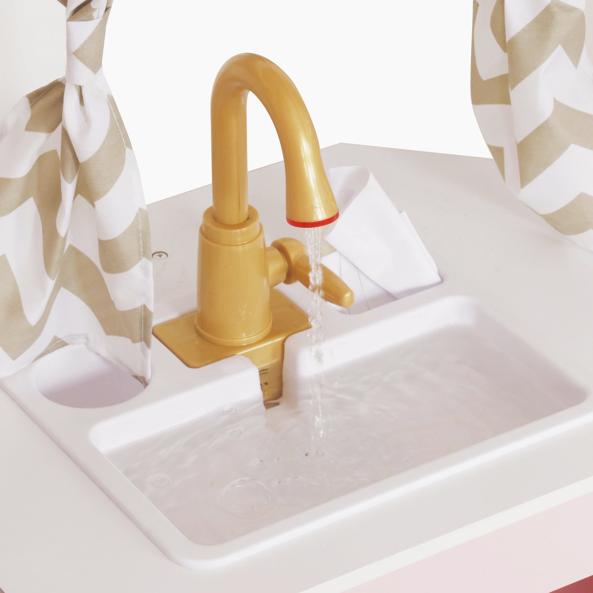 Детайл на мивка с течаща вода към детска ъглова кухня GINGER HOME със златист кран и прозорец със завеси